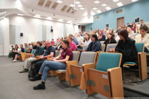Dyktando Uniwersyteckie 2025. Sala wykładowa. Ujęcie bokiem na uczestników konkursu na siedzeniach.